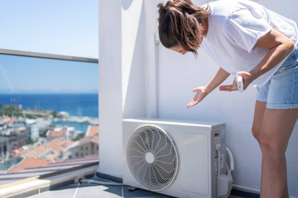 mujer inspeccionando unidad exterior de aire acondicionado en terraza en verano