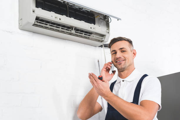 técnico sonriente hablando por teléfono mientras repara unidad interior de aire acondicionado